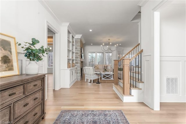 foyer featuring ornamental molding, light wood-type flooring, a chandelier, and visible vents