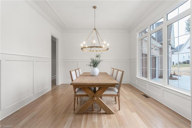 dining room with light wood finished floors, visible vents, a decorative wall, and a notable chandelier