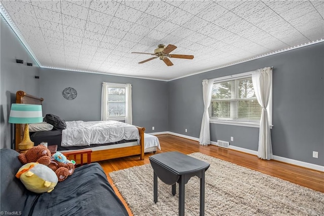 bedroom with visible vents, wood finished floors, crown molding, baseboards, and ceiling fan