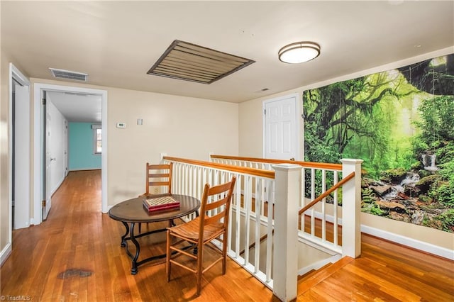 corridor with an upstairs landing, visible vents, baseboards, and wood finished floors