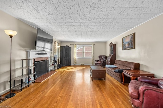 living room featuring a brick fireplace, baseboards, crown molding, and light wood-style floors