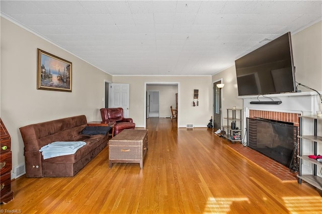 living area featuring visible vents, a brick fireplace, baseboards, ornamental molding, and light wood-style flooring