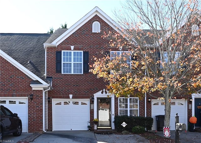 traditional-style home featuring roof with shingles, a garage, driveway, and brick siding