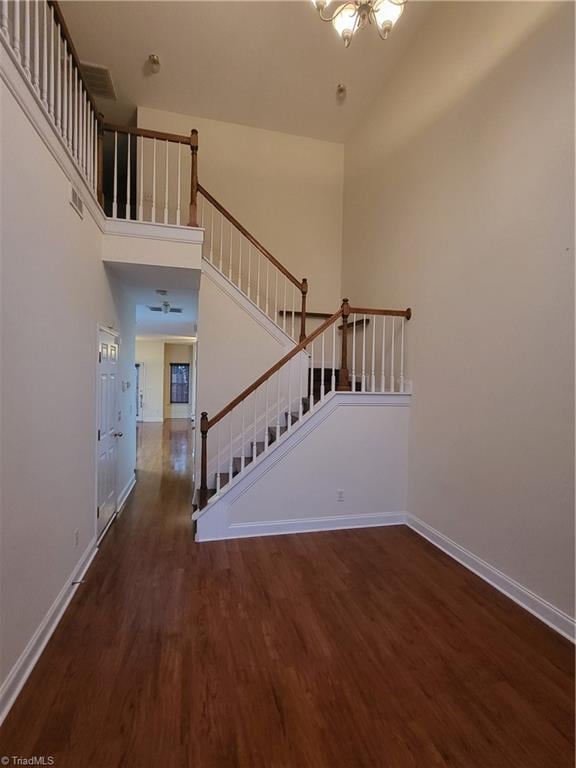 stairway with baseboards, a high ceiling, wood finished floors, and a notable chandelier