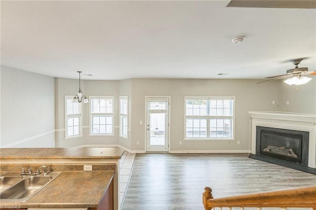 unfurnished living room featuring wood-type flooring, sink, and ceiling fan with notable chandelier