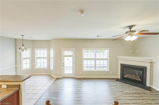 unfurnished living room featuring ceiling fan with notable chandelier and light wood-type flooring