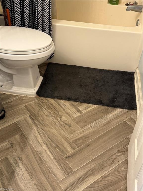 bathroom featuring shower / bath combination with curtain, hardwood / wood-style flooring, and toilet