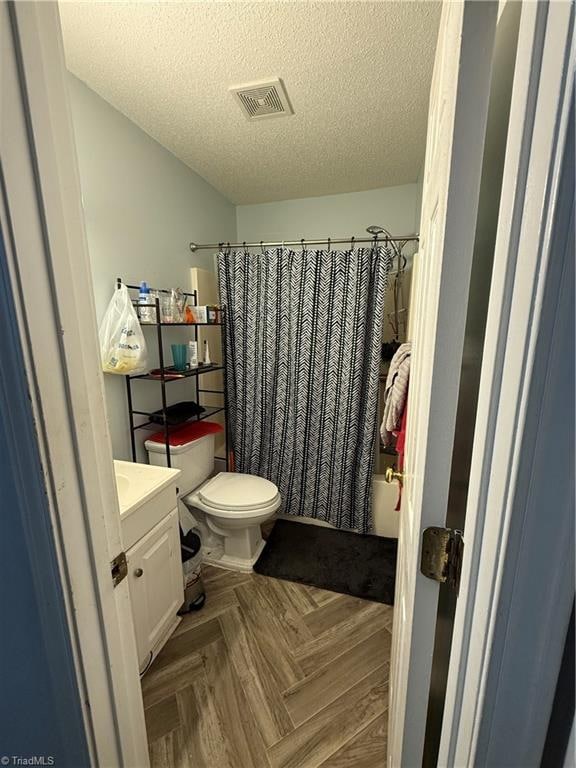 bathroom with parquet flooring, walk in shower, a textured ceiling, vanity, and toilet