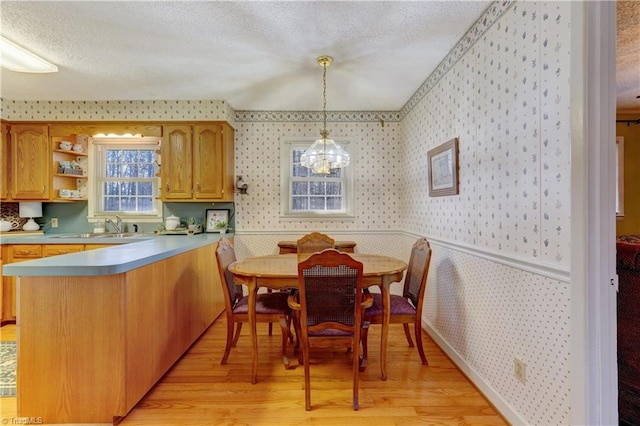 kitchen featuring wallpapered walls, a wainscoted wall, a peninsula, a textured ceiling, and light wood-type flooring