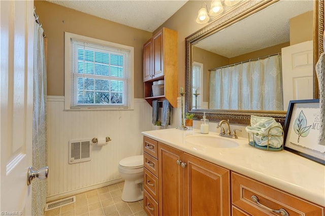 bathroom featuring a textured ceiling, toilet, vanity, visible vents, and wainscoting