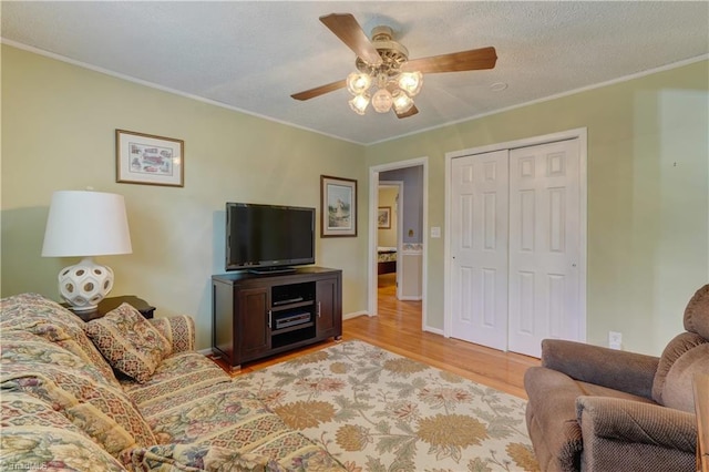 living room with ornamental molding, light wood-type flooring, a ceiling fan, and baseboards