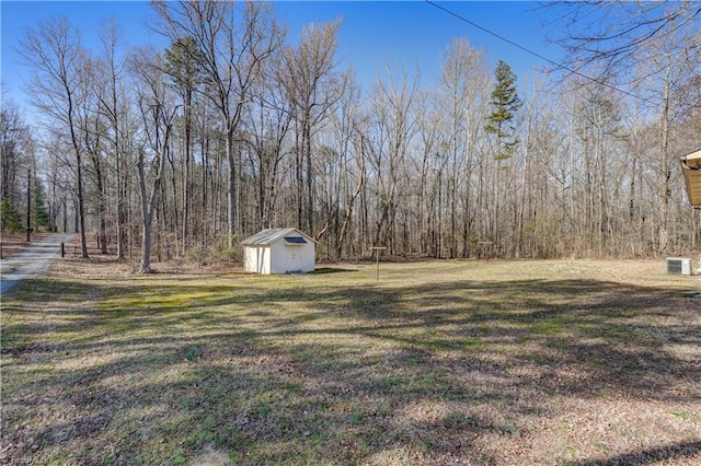 view of yard with a forest view, a storage unit, and an outbuilding