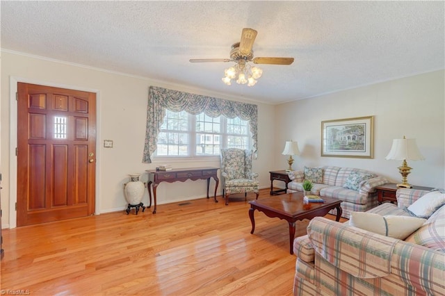 living room featuring a textured ceiling, ceiling fan, baseboards, light wood finished floors, and crown molding