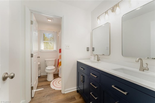 full bathroom with toilet, double vanity, a sink, and wood finished floors