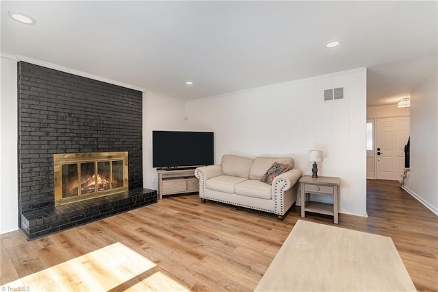 living area with crown molding, recessed lighting, visible vents, a brick fireplace, and wood finished floors