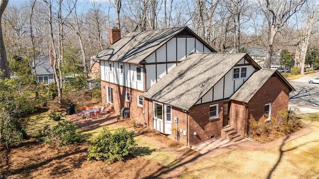 rear view of property with driveway, a shingled roof, a chimney, and brick siding