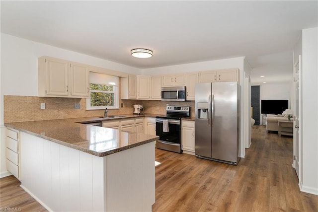 kitchen with stone counters, a peninsula, a sink, light wood-style floors, and appliances with stainless steel finishes