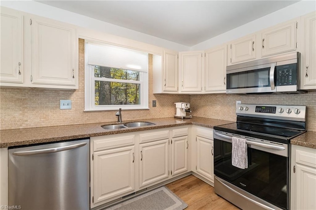 kitchen featuring a sink, light wood-style floors, appliances with stainless steel finishes, backsplash, and dark countertops