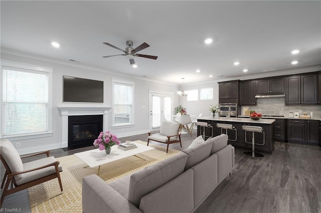 living room with crown molding, dark hardwood / wood-style flooring, and ceiling fan with notable chandelier