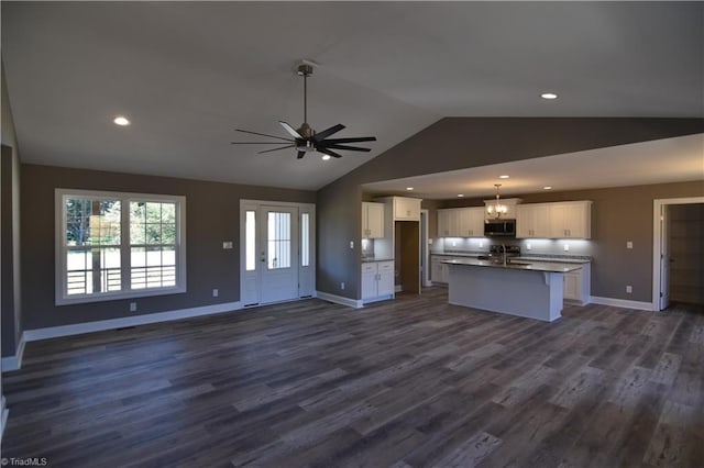 kitchen featuring an island with sink, lofted ceiling, white cabinets, dark wood-type flooring, and ceiling fan with notable chandelier