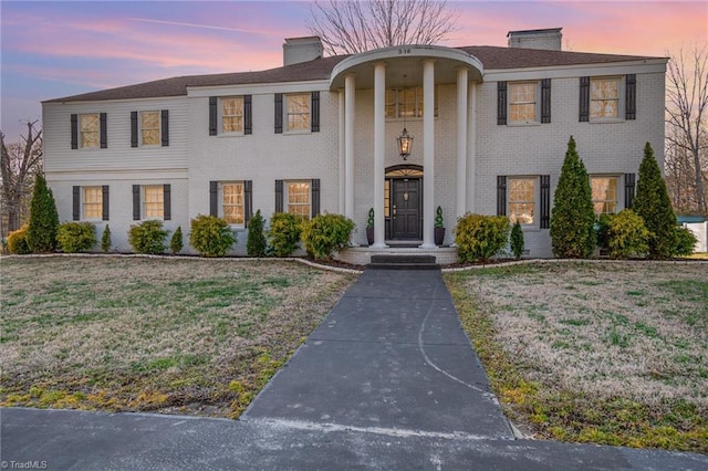 neoclassical / greek revival house featuring brick siding, a chimney, and a lawn