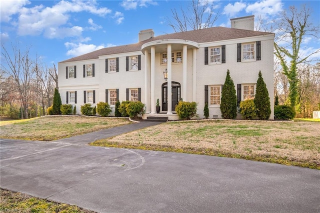 neoclassical home featuring brick siding, crawl space, a chimney, and a front lawn