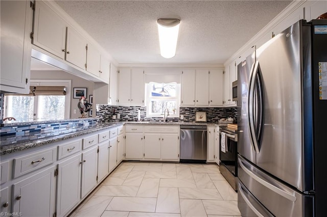 kitchen with a sink, white cabinetry, appliances with stainless steel finishes, backsplash, and dark stone countertops