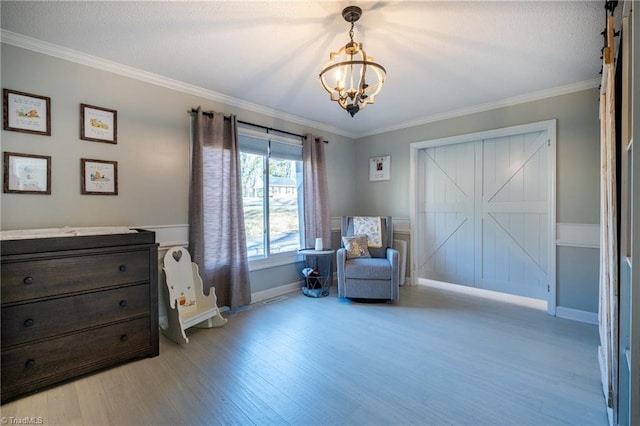 sitting room featuring a barn door, baseboards, crown molding, light wood-type flooring, and a chandelier