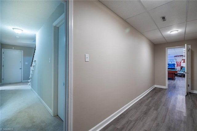 hallway with a paneled ceiling, visible vents, baseboards, and wood finished floors