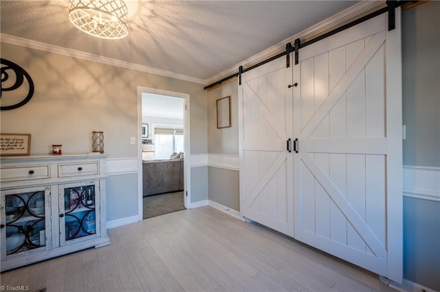 interior space featuring ornamental molding, light wood-type flooring, a textured ceiling, and a barn door