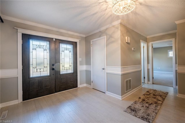 foyer featuring light wood finished floors, visible vents, crown molding, and french doors