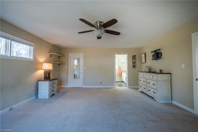 interior space featuring a ceiling fan, ensuite bath, light colored carpet, and baseboards