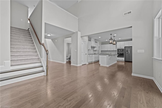 unfurnished living room featuring visible vents, a sink, dark wood finished floors, stairway, and baseboards