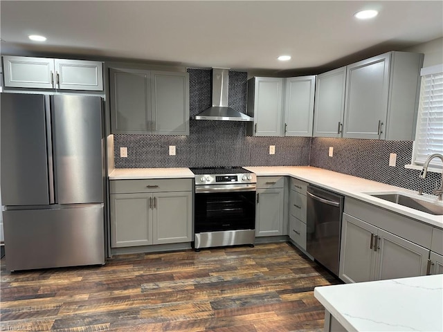 kitchen featuring dark wood-type flooring, gray cabinets, a sink, stainless steel appliances, and wall chimney exhaust hood