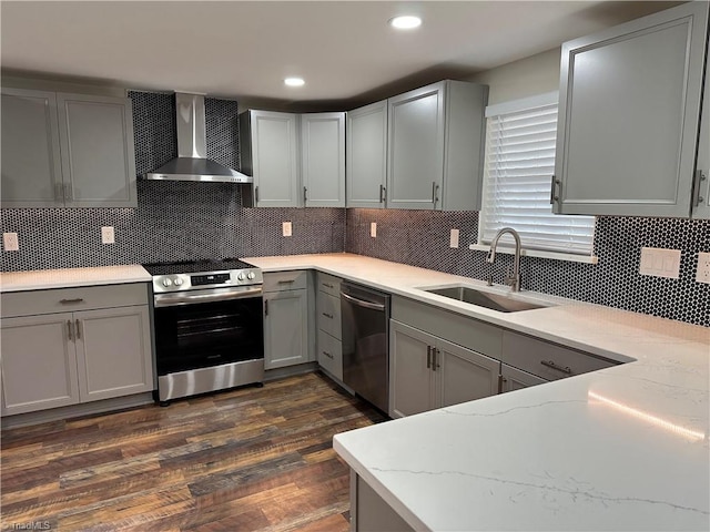 kitchen featuring light stone countertops, gray cabinets, stainless steel appliances, wall chimney exhaust hood, and a sink