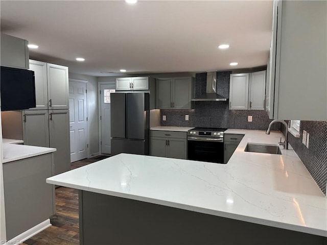 kitchen featuring electric stove, a sink, light stone counters, freestanding refrigerator, and wall chimney range hood