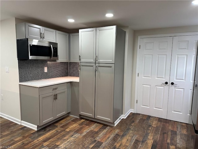 kitchen featuring dark wood finished floors, gray cabinetry, light countertops, stainless steel microwave, and backsplash