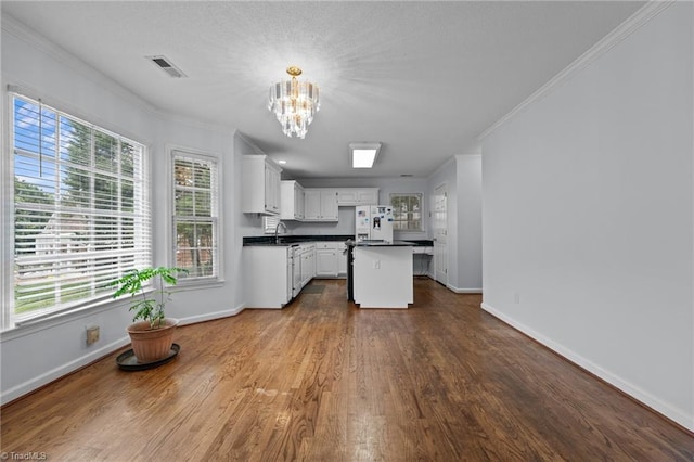 kitchen featuring dark countertops, a chandelier, ornamental molding, and white refrigerator with ice dispenser