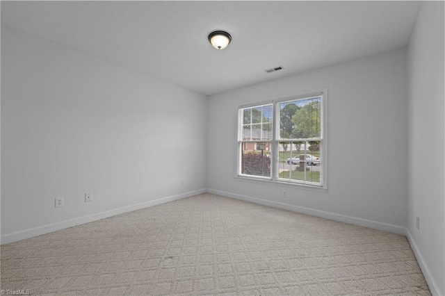 spare room featuring baseboards, light colored carpet, and visible vents