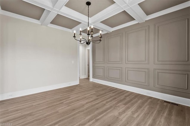 unfurnished dining area featuring baseboards, coffered ceiling, a decorative wall, a notable chandelier, and light wood-type flooring