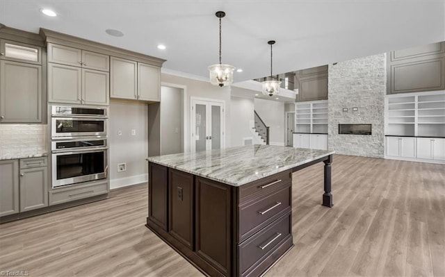 kitchen with light wood-type flooring, decorative light fixtures, french doors, double oven, and crown molding