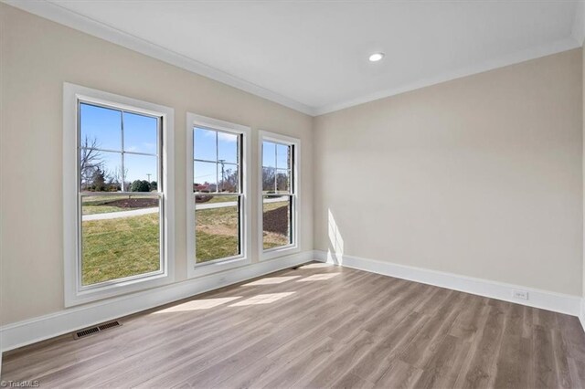 spare room featuring visible vents, wood finished floors, baseboards, and ornamental molding