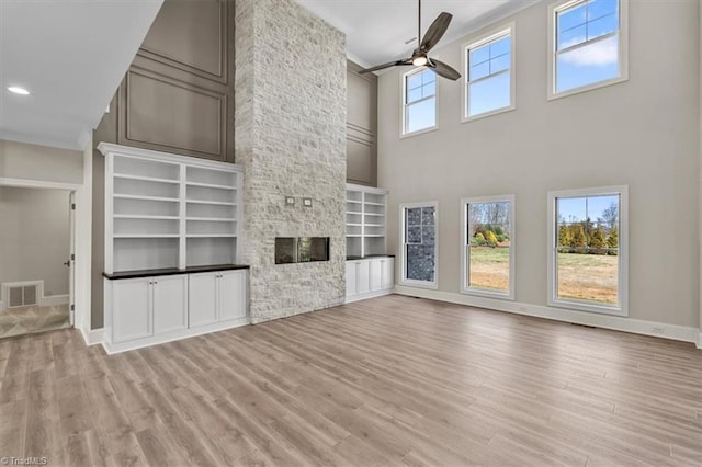 unfurnished living room featuring visible vents, a stone fireplace, wood finished floors, and a ceiling fan