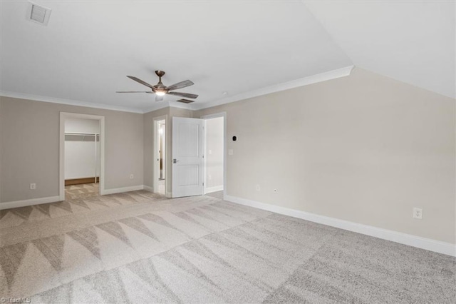 unfurnished bedroom featuring a walk in closet, ornamental molding, a ceiling fan, baseboards, and light colored carpet