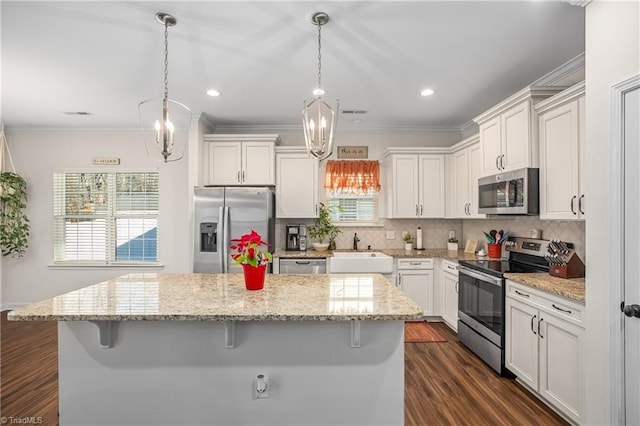 kitchen with appliances with stainless steel finishes, a breakfast bar, sink, decorative light fixtures, and a kitchen island