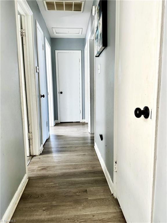 hallway with visible vents, baseboards, and wood finished floors