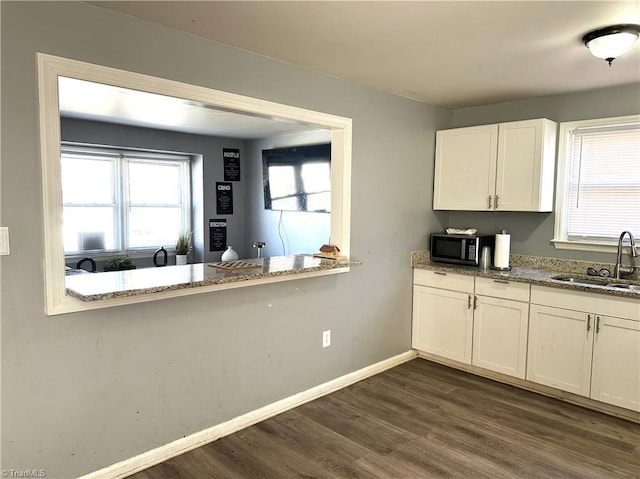 kitchen with a sink, dark wood finished floors, white cabinets, baseboards, and light stone countertops