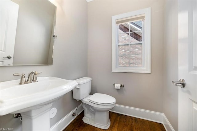 half bath featuring baseboards, a sink, toilet, and wood finished floors