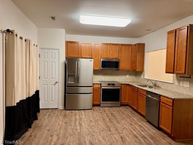 kitchen with decorative backsplash, appliances with stainless steel finishes, light hardwood / wood-style flooring, and sink