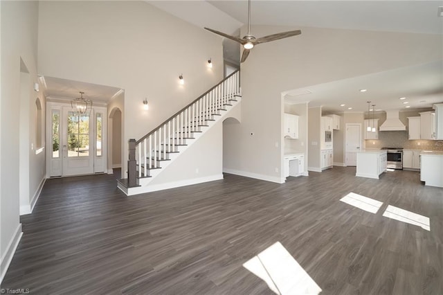 unfurnished living room featuring dark wood-type flooring, high vaulted ceiling, and ceiling fan with notable chandelier